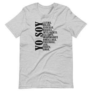 Puede incluir: Una camiseta gris con texto negro que dice "YO SOY" verticalmente, seguida de una lista de palabras en espa&ntilde;ol: "LATINA. MUJER. EDUCADA. MAGICA. INTELIGENTE. VALIENTE. INDEPENDIENTE ORGULLOSA. PODEROSA. LEAL. FUERTE. AMOR."