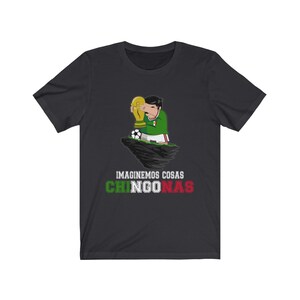 May include: Dark gray t-shirt featuring a cartoon character in a green and white soccer uniform holding a trophy. A soccer ball is at the character's feet. The text "IMAGINEMOS COSAS CHINGONAS" is printed below the character in white, green, and red.
