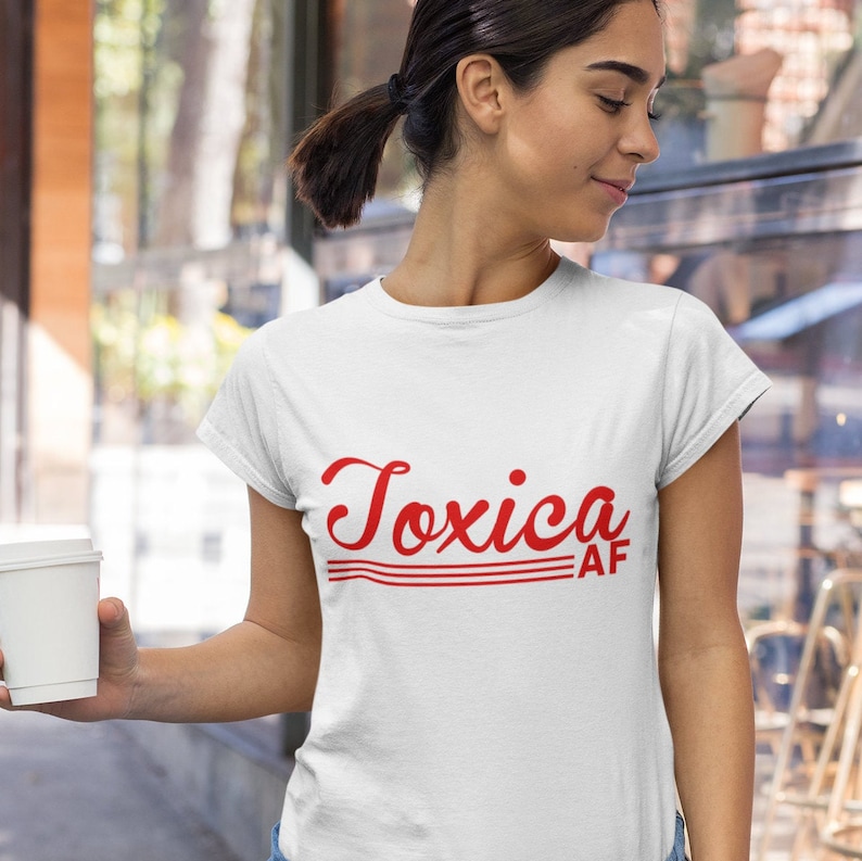 May include: White t-shirt with red text that says "Toxica AF" in a retro font.