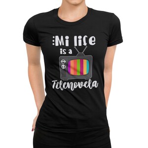 May include: Black t-shirt with white text that reads "Mi life is a telenovela" and a cartoon image of a retro television with a rainbow screen.