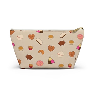 May include: A beige zippered pouch with a repeating pattern of various pastries and sweets, including heart-shaped cookies, croissants, and pig-shaped candies.