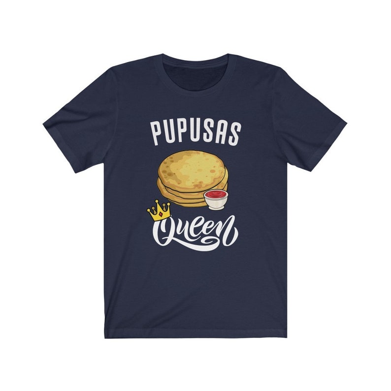 Puede incluir: Una camiseta azul marino con el texto "Pupusas Queen" en letras blancas. Una imagen de dibujos animados de pupusas con un lado de salsa est&aacute; por encima del texto. Una corona dorada est&aacute; a la izquierda del texto.