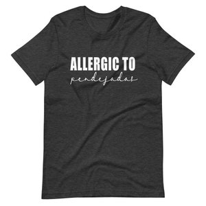 May include: Dark heather grey t-shirt with white text that reads "ALLERGIC TO pendejadas".