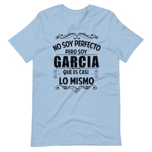 May include: Light blue t-shirt with black text that reads "No soy perfecto pero soy Garcia que es casi lo mismo" which translates to "I am not perfect but I am Garcia which is almost the same".