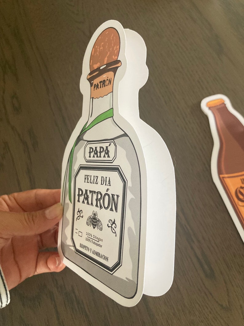May include: White card shaped like a Patron tequila bottle with the text "Pap&aacute; Feliz D&iacute;a Patr&oacute;n 100% Ching&oacute;n 100% Trabajador Respeto y Admiraci&oacute;n"