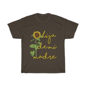 Puede incluir: Una camiseta marr&oacute;n con un gr&aacute;fico de girasol y el texto "hija de mi madre" en amarillo.