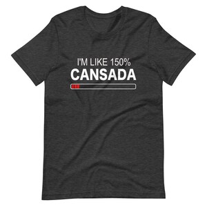 May include: A dark heather grey t-shirt with white text that reads "I'm like 150% Cansada" with a progress bar underneath. The progress bar is filled with red.