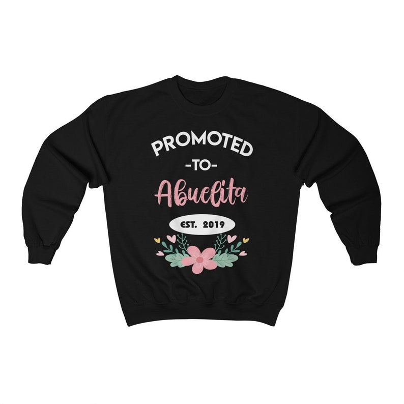 May include: Black sweatshirt with the text "PROMOTED -to- Abuelita EST. 2019" in white and pink lettering. The design includes a floral arrangement with pink flowers and green leaves.