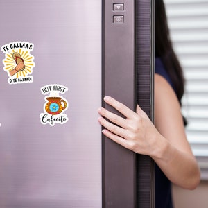 May include: Three refrigerator magnets with colorful designs and Spanish phrases. The magnets feature illustrations of a coffee cup, a pot of beans, and a flip-flop.