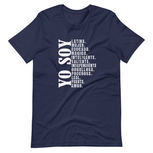 Puede incluir: Camiseta azul marino con texto blanco que dice "YO SOY" y una lista de atributos positivos en espa&ntilde;ol. El texto incluye "Latina, Mujer, Educada, Magica, Inteligente, Valiente, Independiente, Orgullosa, Poderosa, Leal, Fuerte, Amor."