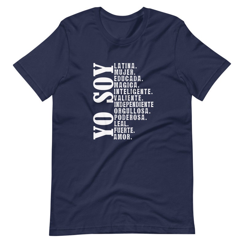 Puede incluir: Camiseta azul marino con texto blanco que dice "YO SOY" y una lista de atributos positivos en espa&ntilde;ol. El texto incluye "Latina, Mujer, Educada, Magica, Inteligente, Valiente, Independiente, Orgullosa, Poderosa, Leal, Fuerte, Amor."