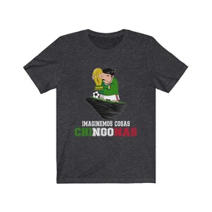 May include: Dark gray t-shirt featuring a cartoon illustration of a person in a green and white soccer uniform holding a golden trophy. A soccer ball is at their feet. The text "IMAGINEMOS COSAS CHINGONAS" is below the illustration.