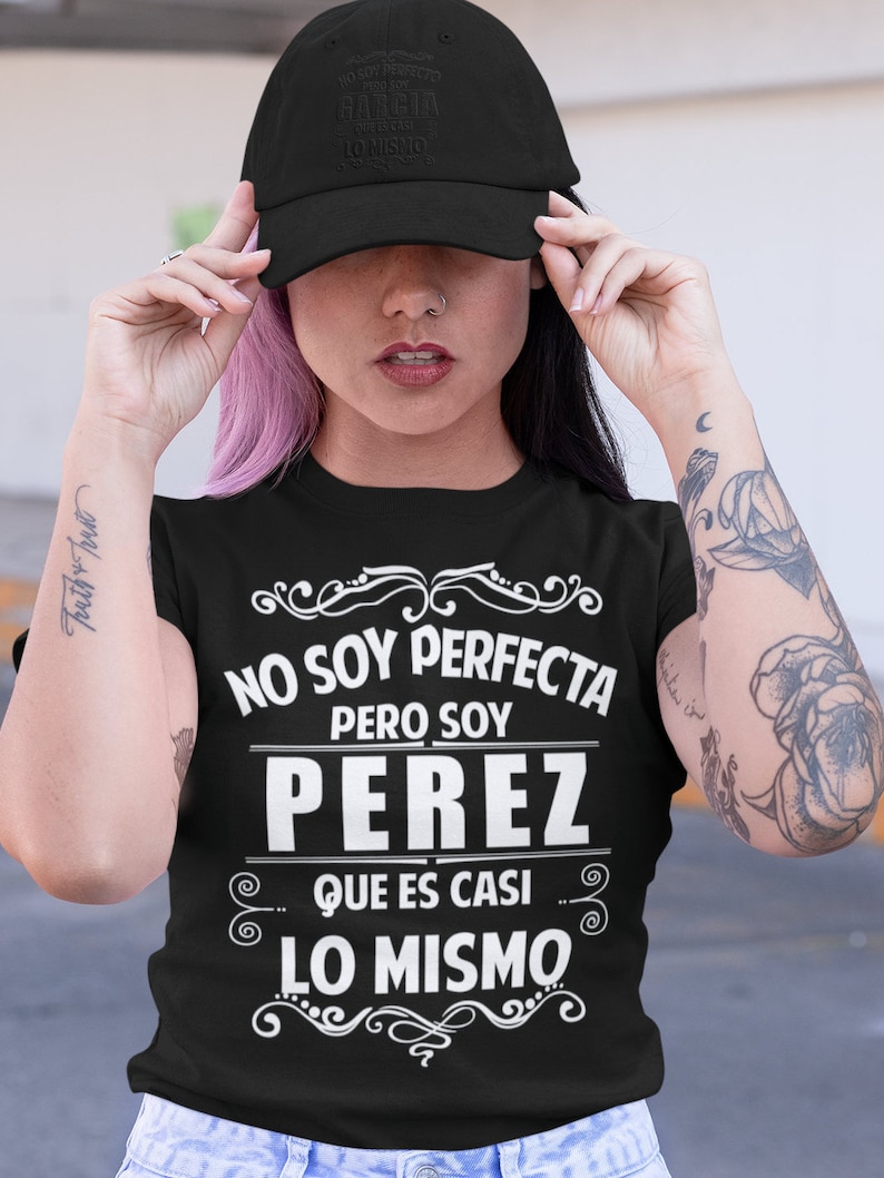 May include: Black t-shirt with white text that reads "NO SOY PERFECTA PERO SOY PEREZ QUE ES CASI LO MISMO". The text is surrounded by decorative swirls.