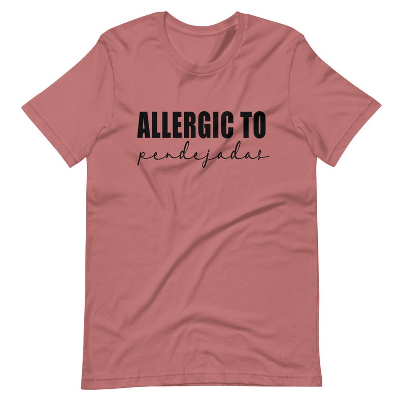 May include: A pink t-shirt with the text "ALLERGIC TO pendejadas" in black.