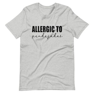 May include: A heather grey t-shirt with black text that reads "ALLERGIC TO pendejadas".
