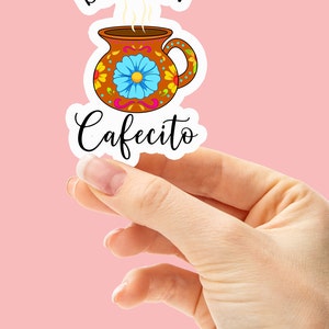 May include: A sticker with a brown coffee mug with colorful floral designs and the text "BUT FIRST Cafecito" in black.