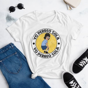 May include: White t-shirt with a yellow circle graphic featuring a cartoon character dancing and the text "Yo Perreo Sola" repeated twice.