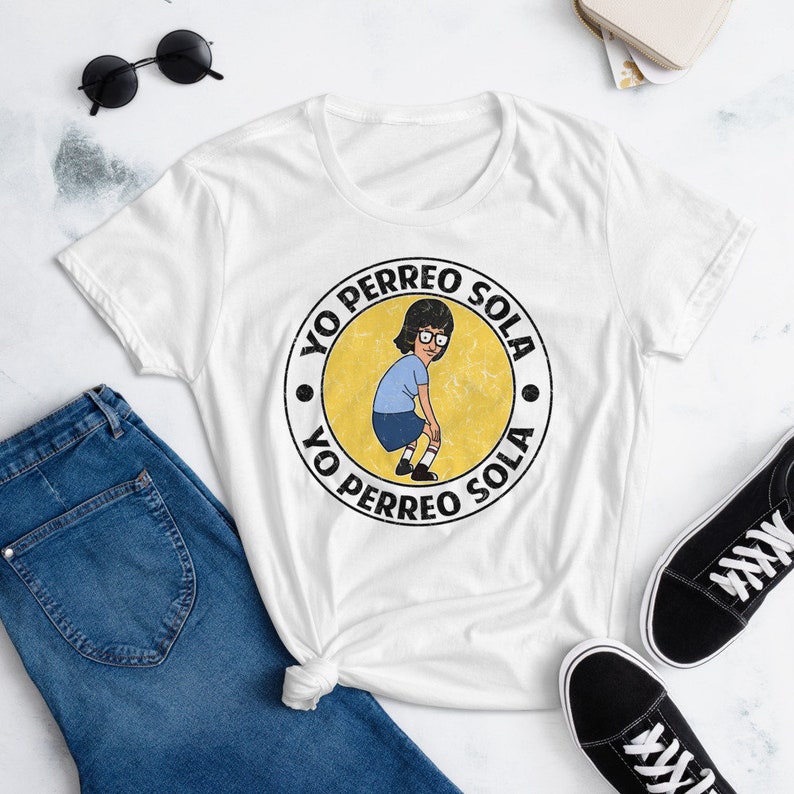May include: White t-shirt with a yellow circle graphic featuring a cartoon character dancing and the text "Yo Perreo Sola" repeated twice.