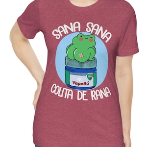 May include: Maroon t-shirt featuring a cartoon frog sitting on a VapoR&uacute; jar. The frog is green with a bandage, and the text reads "Sana Sana Colita de Rana". The design is in a blue circle.