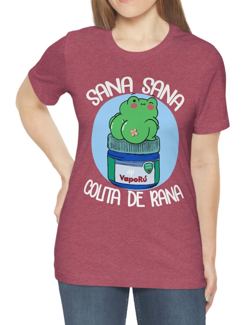 May include: Maroon t-shirt featuring a cartoon frog sitting on a VapoR&uacute; jar. The frog is green with a bandage, and the text reads "Sana Sana Colita de Rana". The design is in a blue circle.