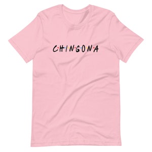 May include: Pink t-shirt with the text "CHINGONA" in black letters with colorful dots between each letter.