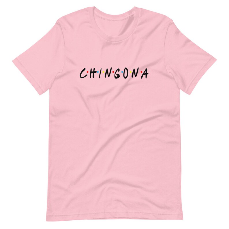 May include: Pink t-shirt with the text "CHINGONA" in black letters with colorful dots between each letter.