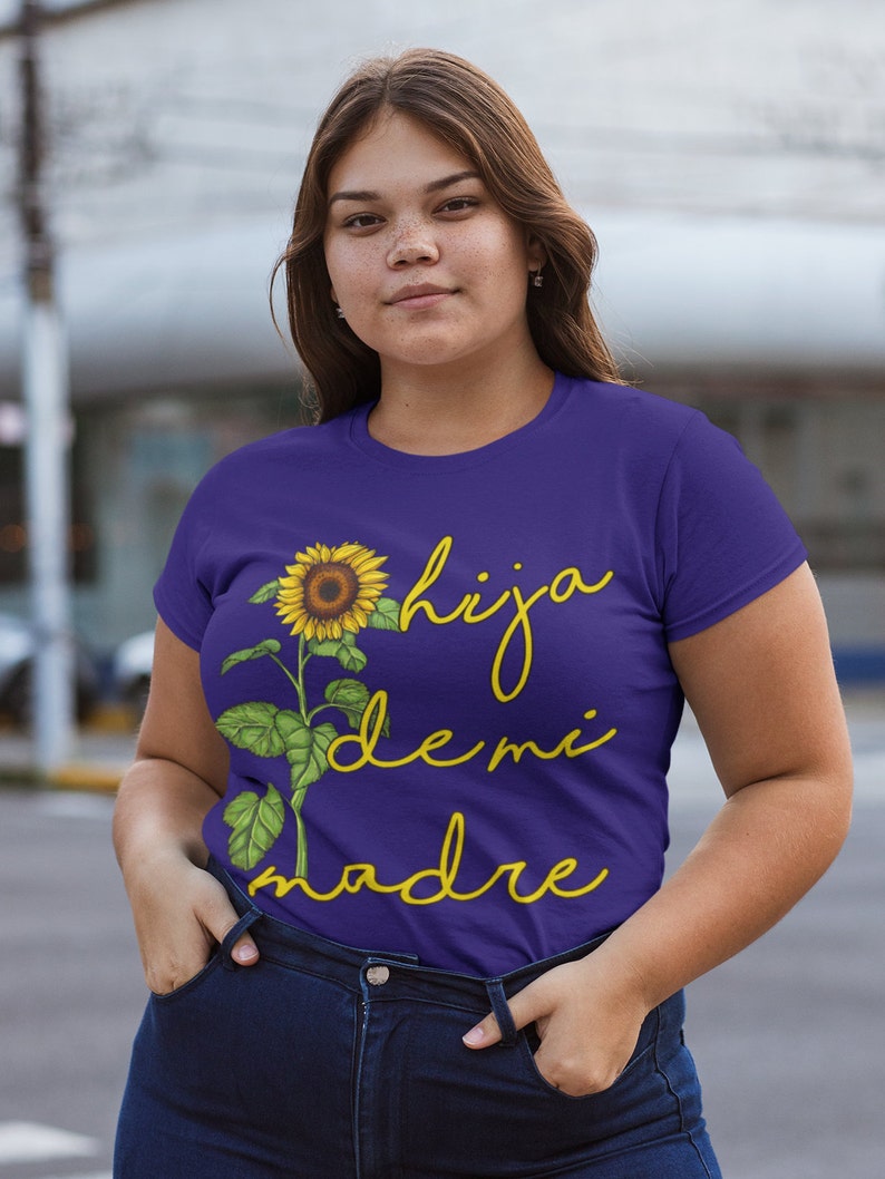 Puede incluir: Camiseta morada con un gr&aacute;fico de girasol y el texto "hija de mi madre" en amarillo.