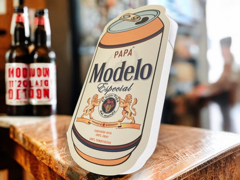 May include: A white and orange can with a brown label. The label has the text "Modelo Especial" in a brown font with the words "Pap&aacute;" above it. The label also has a crest with a lion and the text "El Mejor  Fondo del Mundo".
