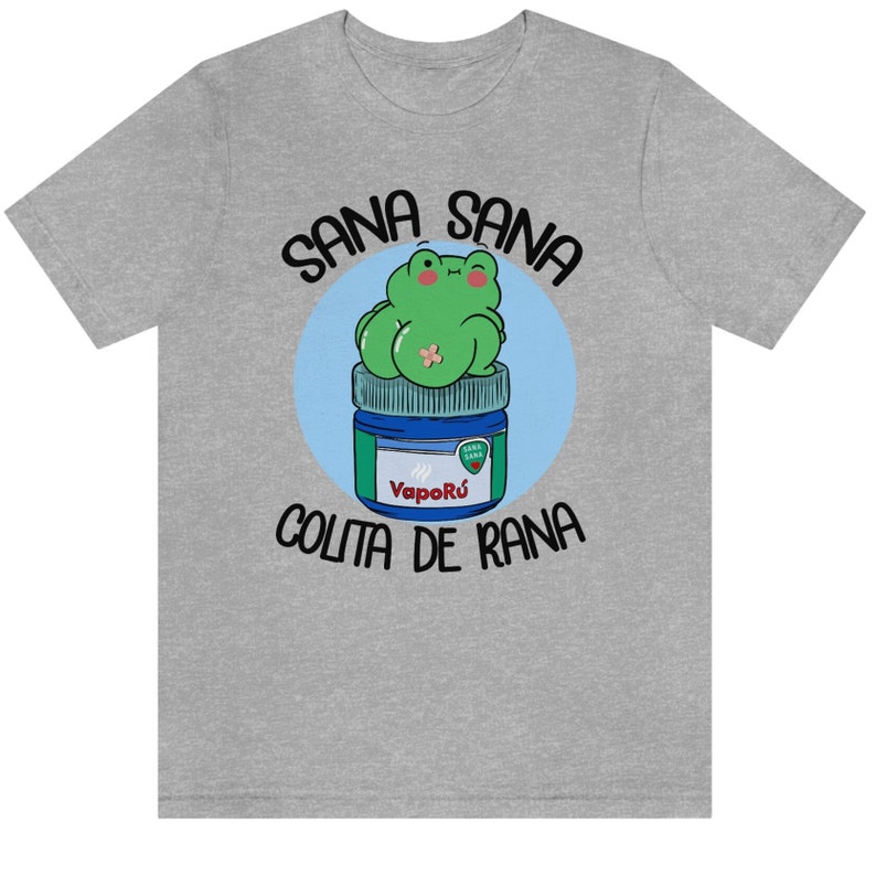 May include: A heather gray t-shirt featuring a cartoon frog sitting on a blue and green jar of VapoR&uacute;. The text "Sana Sana" is arched above the frog, and "Colita de Rana" is arched below.