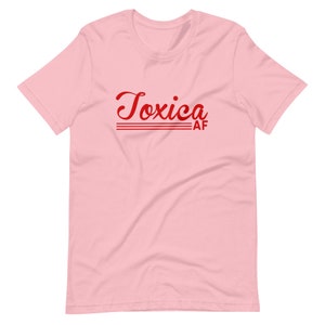 May include: Pink short-sleeved t-shirt with the text "Toxica AF" in red cursive lettering.
