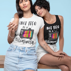 May include: Two people wearing matching shirts with a retro television graphic and the text "Mi life is a Tele" and "novela" on one shirt and "Telemove" on the other. The person on the left is wearing a white shirt and a denim skirt. The person on the right is wearing a black tank top and white denim shorts.