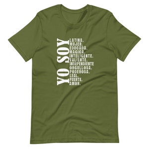 Puede incluir: Una camiseta verde con texto blanco que dice "YO SOY" y una lista de palabras en espa&ntilde;ol que describen a una mujer latina. Las palabras incluyen "Latina, Mujer, Educada, Magica, Inteligente, Valiente, Independiente, Orgullosa, Poderosa, Leal, Fuerte, Amor."