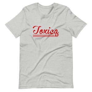 May include: A heather grey t-shirt with the text "Toxica AF" in red cursive lettering.