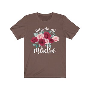 May include: A brown t-shirt with a floral design and the text "Hija de mi madre" in white.