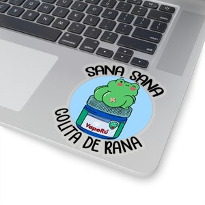 May include: A round sticker with a blue background and a green frog sitting on top of a blue jar with the text "Sana Sana Colita de Rana" and "VapoRu" on it.