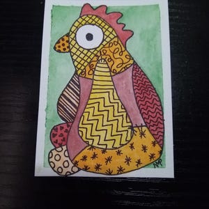 May include: A colorful watercolor painting of a stylized chicken. The chicken features a patchwork design with various patterns and colors, including yellow, orange, red, and brown. The background is a light green wash.