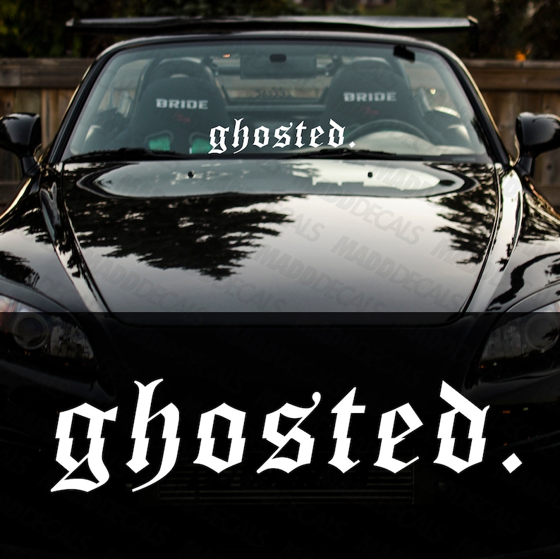 以下が含まれることがあります： 白いゴシック体の「ghosted.」という文字がフロントガラスに書かれた黒いスポーツカー。車のボンネットには周囲の環境が映り込んでいる。車内のシートには「BRIDE」の文字がある。