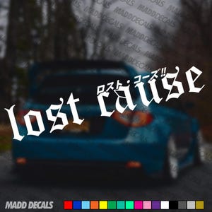May include: White vinyl decal featuring the words "lost cause" in a gothic font, with Japanese text above. The decal is shown on the rear of a blue car. The brand name "MADD DECALS" is at the bottom.