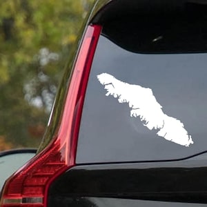 Peut inclure: Un autocollant en vinyle blanc représentant une masse terrestre, probablement une île ou une péninsule, est apposé sur la vitre arrière d'une voiture noire. L'autocollant a une forme irrégulière avec un littoral détaillé. Le feu arrière rouge de la voiture est visible.