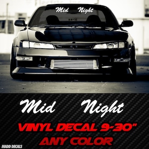 May include: Black sports car with the words "Mid Night" in white script across the windshield. Below, the text "VINYL DECAL 9-30" ANY COLOR" is displayed in red. The car has a low profile and a front air dam.