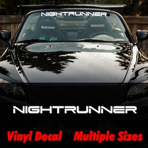 May include: A black convertible car with the text "NIGHTRUNNER" in white across the top of the windshield and on the hood. Below the hood text, the words "Vinyl Decal Multiple Sizes" are in red.