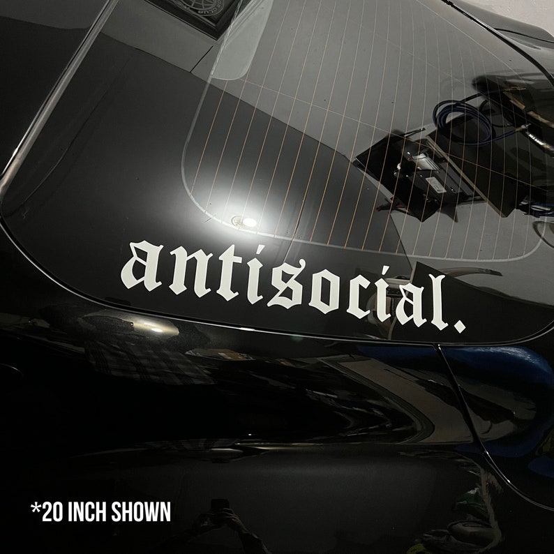 May include: White vinyl decal with the word "antisocial." in a gothic font, affixed to the rear window of a black vehicle. The decal is approximately 20 inches in length. The image shows the decal's placement on the car.