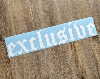 May include: A light blue sticker with the word "exclusive" in a white gothic font. The sticker is rectangular and placed on a wooden surface.