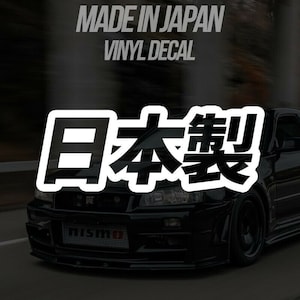 May include: A black vinyl decal featuring the text "MADE IN JAPAN" and "VINYL DECAL" in white. Large white Japanese characters are displayed over a black sports car.