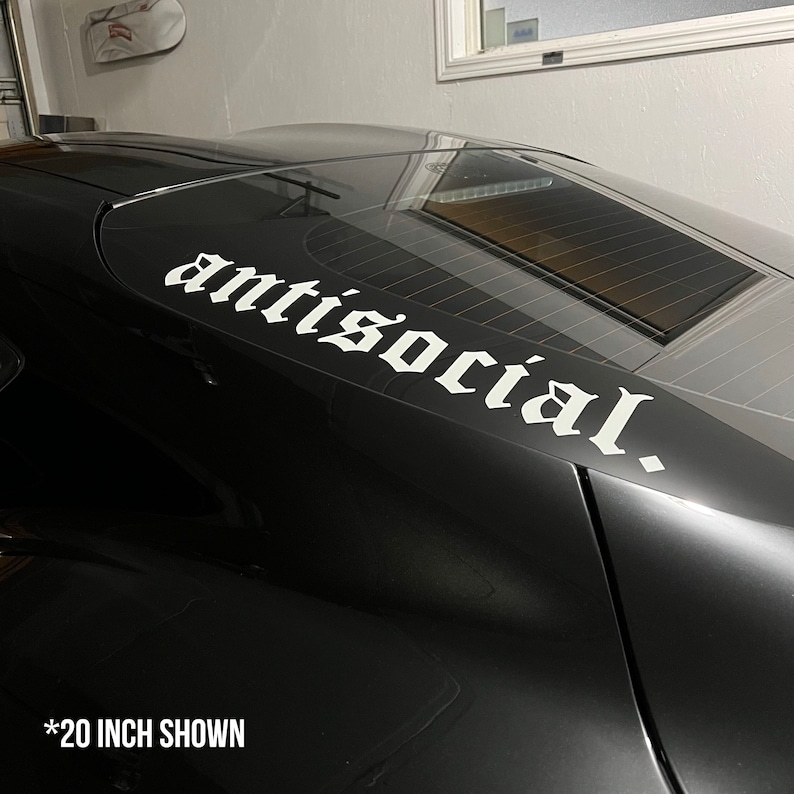 May include: A black car with a white decal that reads "antisocial." The decal is in a gothic font and is approximately 20 inches long. The decal is placed on the rear window of the car.