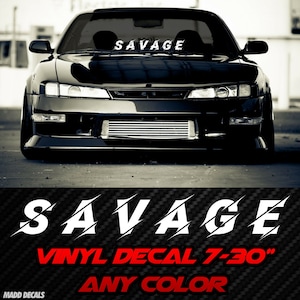 May include: Black sports car with the word "SAVAGE" in white across the windshield. A vinyl decal with the word "SAVAGE" in white with a slash design is displayed below the car. The decal is available in any color.
