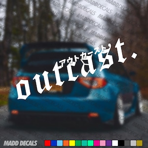 Op de afbeelding: Witte "outcast" sticker met Japanse karakters, aangebracht op de achterkant van een blauwe auto. De sticker is in een gotische letterstijl. De onderkant van de afbeelding toont een kleurenpalet en de tekst "MADD DECALS".