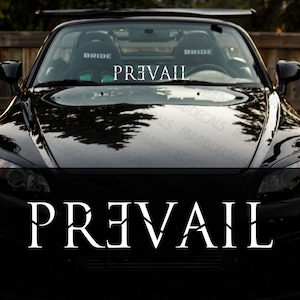 Può includere: Un'auto sportiva nera con la scritta "PREVAIL" in lettere bianche sul cofano. La superficie lucida dell'auto riflette l'ambiente circostante. L'immagine evidenzia il design elegante dell'auto e la decalcomania personalizzata.