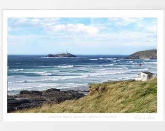 Könnte beinhalten: Ein Foto eines weißen Häuschens auf einer grasbewachsenen Klippe mit Blick auf einen Strand mit tosenden Wellen. In der Ferne ist eine kleine Insel mit einem weißen Leuchtturm zu sehen. Der Himmel ist blau mit weißen Wolken.