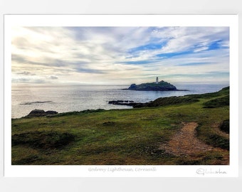 Könnte beinhalten: Ein Foto eines weißen Leuchtturms auf einer kleinen Insel in der Ferne. Der Leuchtturm ist von grünem Gras umgeben und der Ozean befindet sich im Vordergrund. Der Himmel ist blau mit weißen Wolken.